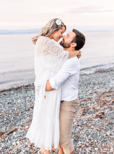 man lifts his bride to be up to kiss her during their beach engagement session