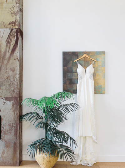 sleek bridal gown hanging from a piece of art next to a fireplace at a lakeside cottage on Vancouver island