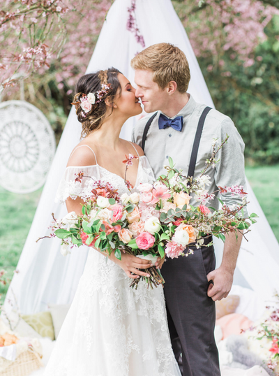 bride and groom kissing in front of a whimsical, boho cherry blossom elopement scene.