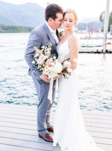 Groom nuzzles bride while standing on a dock over sprout lake on vancouver island