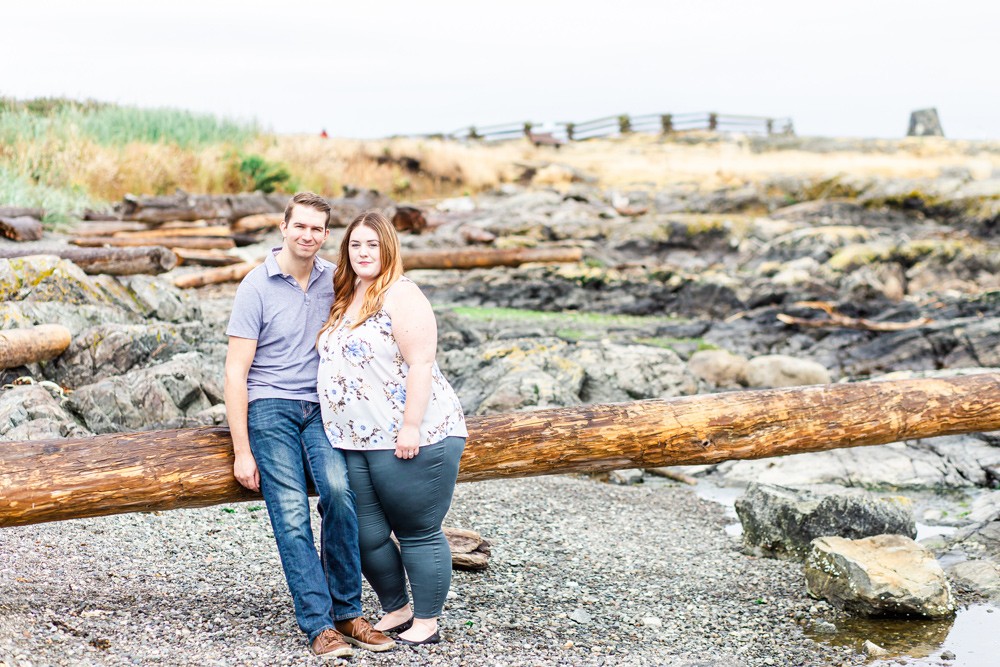 couple leaning on a large driftwood log on a rocky Vancouver island beach